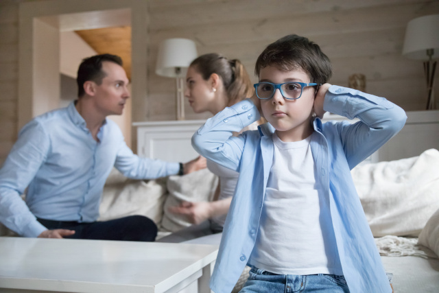 A boy covering his ears with his parents talking behind him child custody